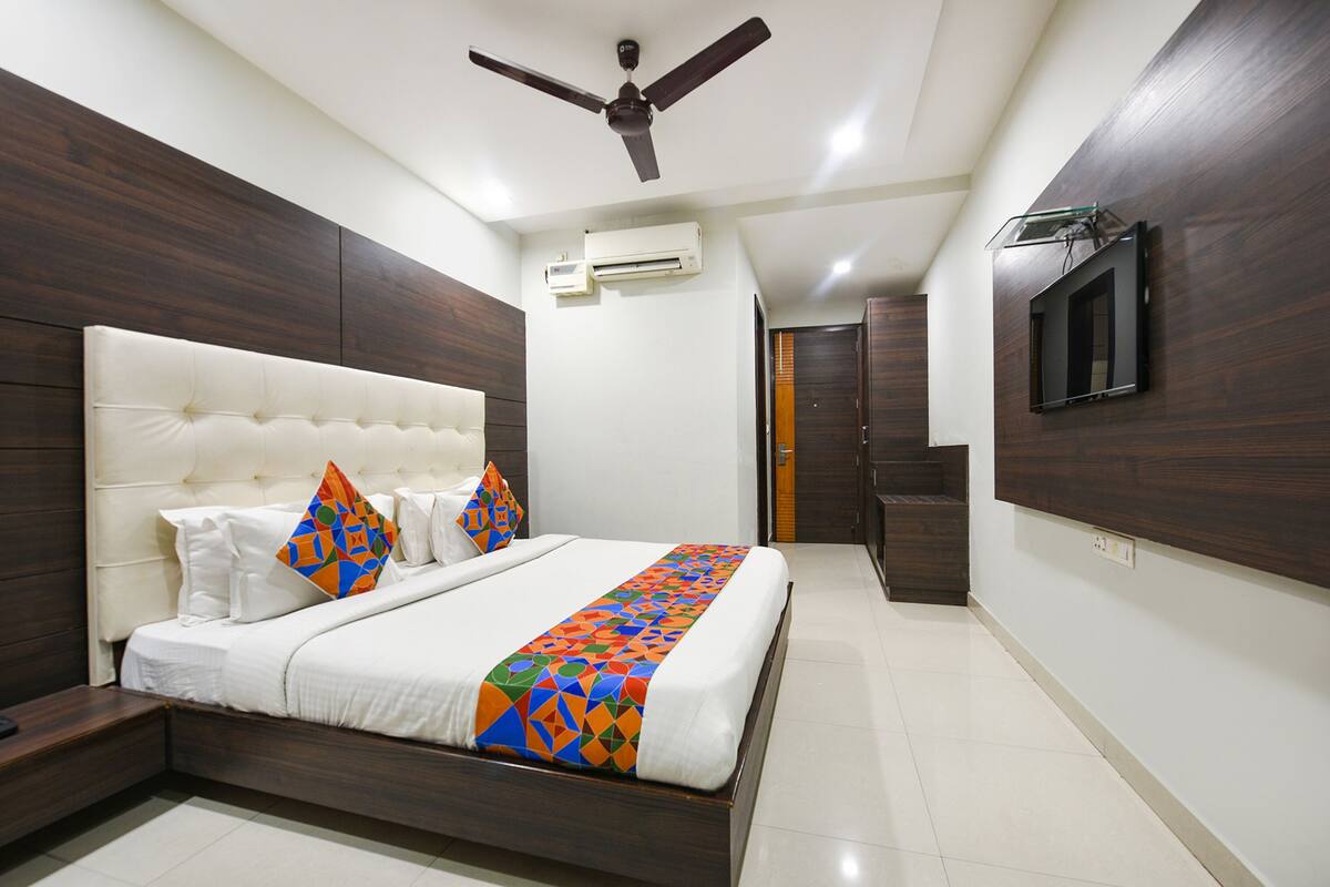 Une chambre moderne avec un grand lit, un ventilateur de plafond, un climatiseur, un téléviseur fixé au mur et une armoire en bois.