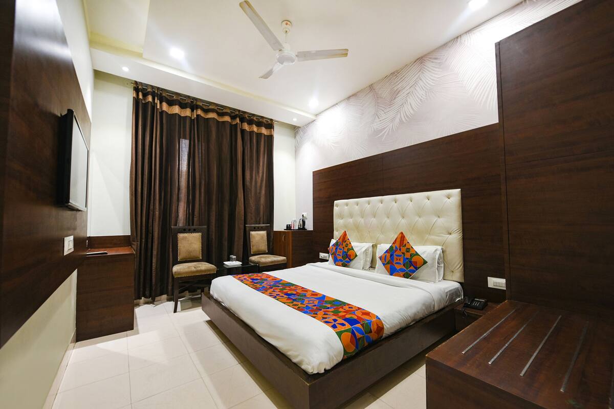 Une chambre d’hôtel avec un grand lit, un bureau, une chaise, une armoire, un ventilateur de plafond et un téléviseur.