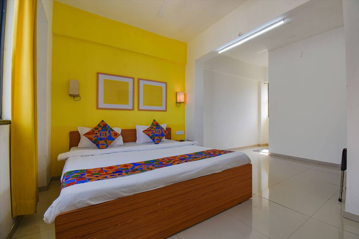 Una habitación de hotel con una cama grande, paredes amarillas y dos cuadros en la pared.