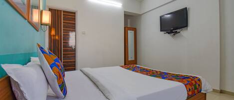 A bedroom with two beds, a television mounted on the wall, and a wooden door.