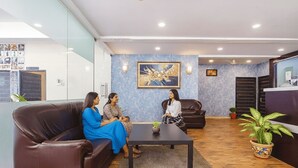 Een receptiegedeelte met een bruine leren bank, een bijzettafeltje en een blauwe muur met een groot schilderij.
