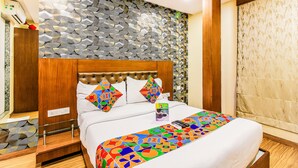 A neatly made bed with a colorful geometric-patterned bedspread, a wooden headboard, and a decorative wall with a leaf-like pattern. - Fabhotel Arton Suite (Mumbai)