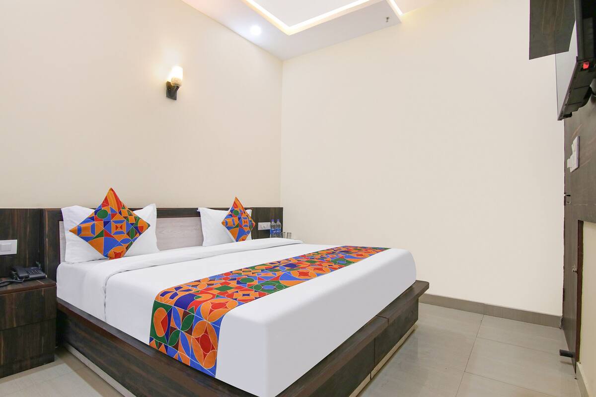 A neatly made bed with a colorful geometric-patterned bedspread, a white pillow, and a matching pillow on a wooden headboard.