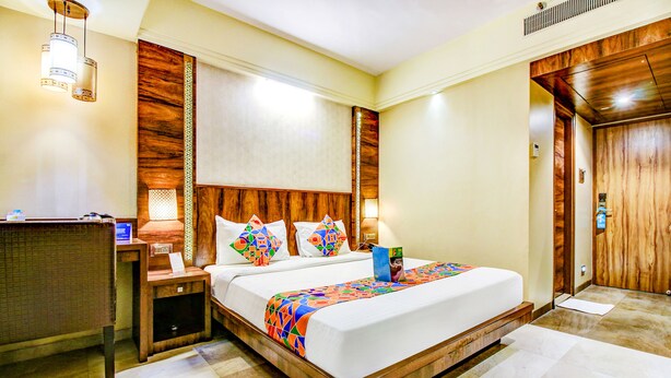Quarto de hotel com uma cama grande, cabeceira de madeira, mesas de cabeceira e uma escrivaninha com abajur.