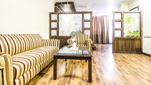 A living room with striped sofas, a glass-top coffee table, and a wooden floor. - FabHotel Aay Kay (Amritsar)
