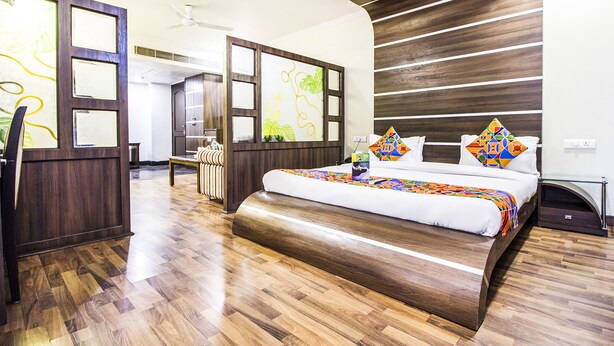 A modern hotel room with a large bed, wooden flooring, a desk, and a bathroom visible through a glass partition. - FabHotel Aay Kay (Amritsar)