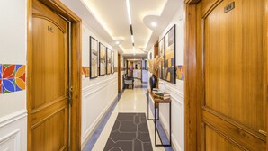 A hotel hallway with wooden doors, a tiled floor, and framed artwork on the walls. - FabHotel Aay Kay (Amritsar)