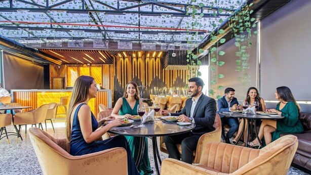 A group of people dining at an outdoor restaurant with a modern design, featuring round tables and comfortable seating. - FabHotel Lake View Topsia (Kolkata)