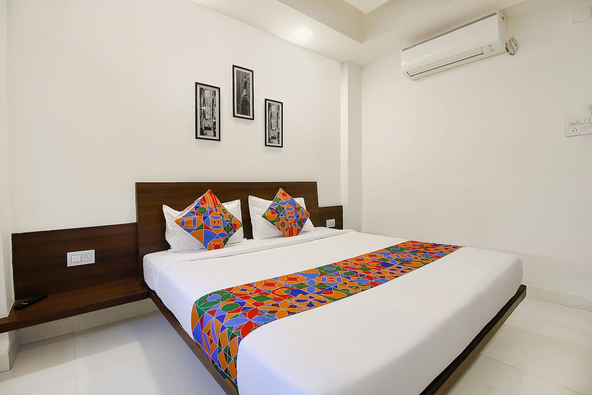 A neatly made bed with a colorful bedspread, a wooden headboard, and two framed pictures on the wall.