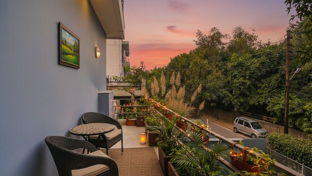 A balcony with wicker chairs and a table, surrounded by potted plants and string lights, overlooking a road with a sunset in the background. - FabHotel F9 Noida Sector 51 (Noida)
