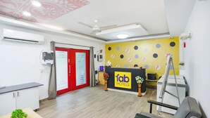 A hotel reception area with a reception desk, a red door, a ceiling fan, and a wall-mounted air conditioner. - FabHotel F9 Noida Sector 51 (Noida)