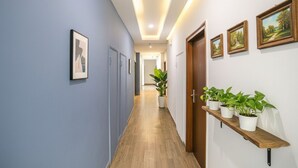 A hallway with a wooden floor, blue walls, and a wooden door. There are potted plants on a shelf and framed pictures on the walls. - FabHotel F9 Noida Sector 51 (Noida)