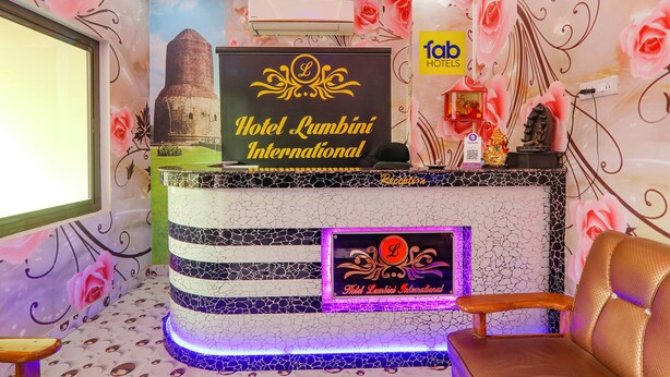 A reception desk with a sign for Hotel Lumbini International, a reception area with a decorative wall, and a seating area with a chair. - FabHotel Lumbini International (Varanasi)