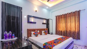 A modern hotel room with a large bed, a flat-screen TV, a bedside table with bottled water, and a bathroom with a shower curtain. - FabHotel Lumbini International (Varanasi)