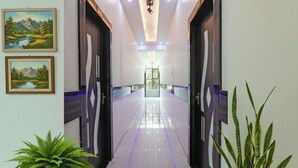 A hallway with a marble floor, framed landscape paintings, and potted plants. - FabHotel Lumbini International (Varanasi)