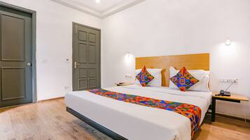 A hotel room with a large bed, two pillows, a bedside table with a phone, and a door.