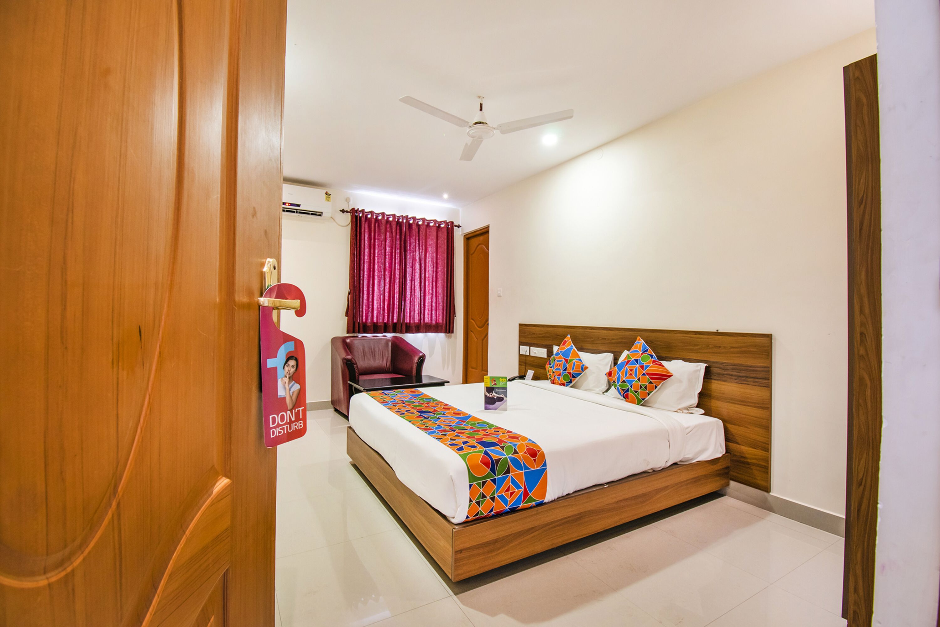 A hotel room with a wooden bed, a ceiling fan, a red chair, and a 'Don't Disturb' sign.
