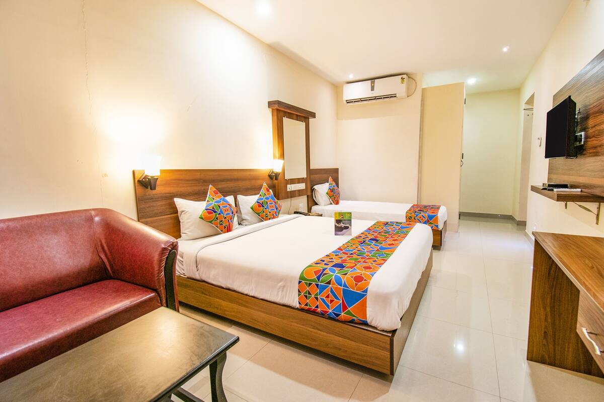Habitación de hotel con una cama de madera, un sofá rojo, una mesita y un televisor montado en la pared.