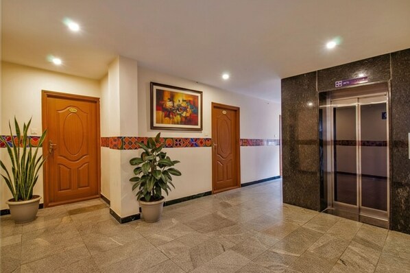 A hotel lobby with a reception desk, two wooden doors, a colorful wall decoration, a potted plant, and an elevator. - Fabhotel Thejas Paaradise (Coimbatore)