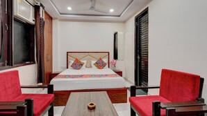 A hotel room with a bed, two red chairs, a wooden table, and a ceiling fan. - FabHotel Metro Inn (Kanpur)