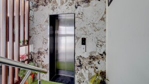 An elevator with a metallic finish, a wall with a marbled pattern, and a railing with potted plants. - FabHotel Metro Inn (Kanpur)