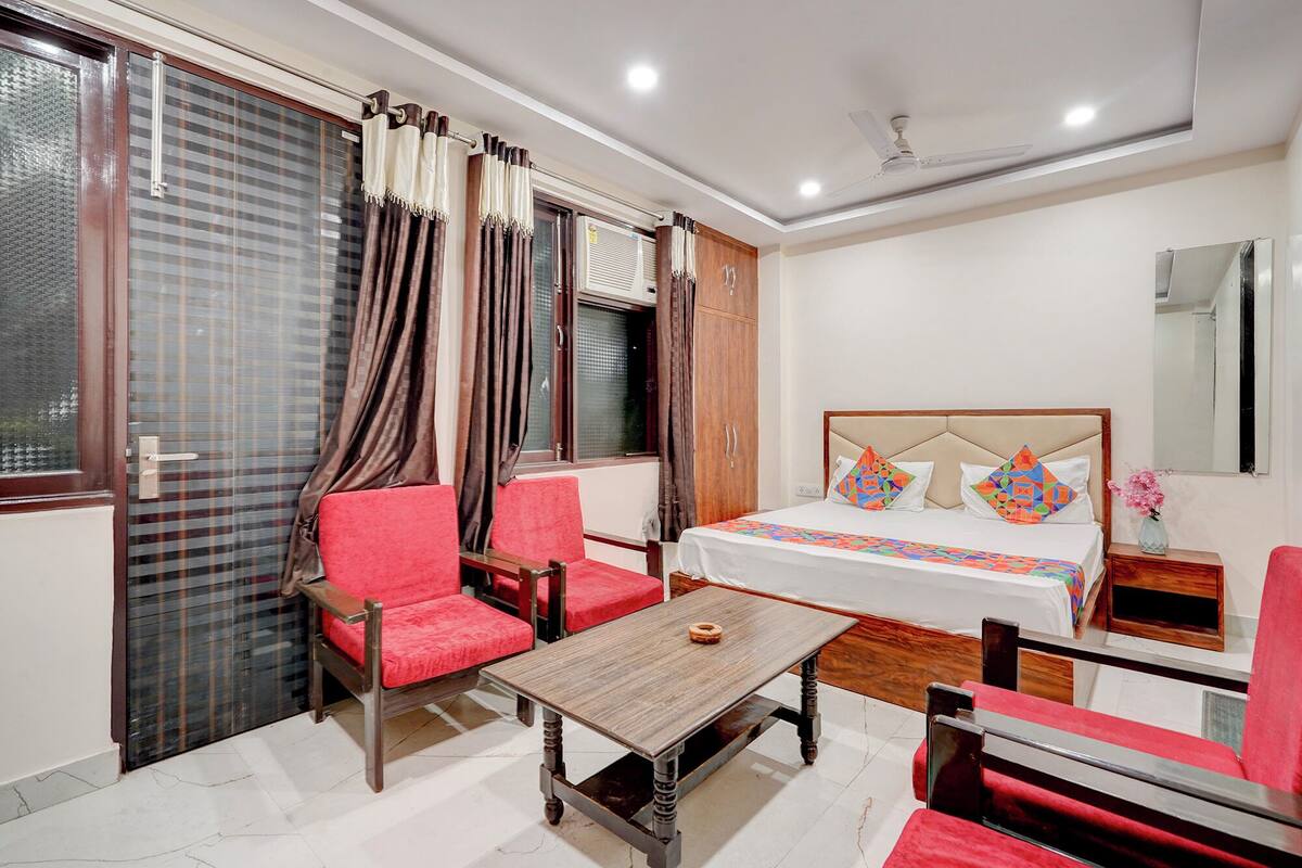 Une chambre d’hôtel avec un lit, deux chaises rouges, une table en bois, une armoire et une fenêtre avec des rideaux.