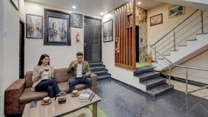 A lobby with a staircase, a coffee table with a book and a cup, and two people sitting on a couch. - FabHotel Metro Inn (Kanpur)