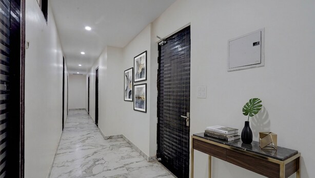 A hallway with a marble floor, a black door, framed pictures on the wall, and a console table with books and a vase. - FabHotel Metro Inn (Kanpur)