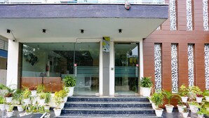 Entrada de un edificio con puerta de vidrio, escalones que conducen a ella y plantas en macetas a ambos lados.