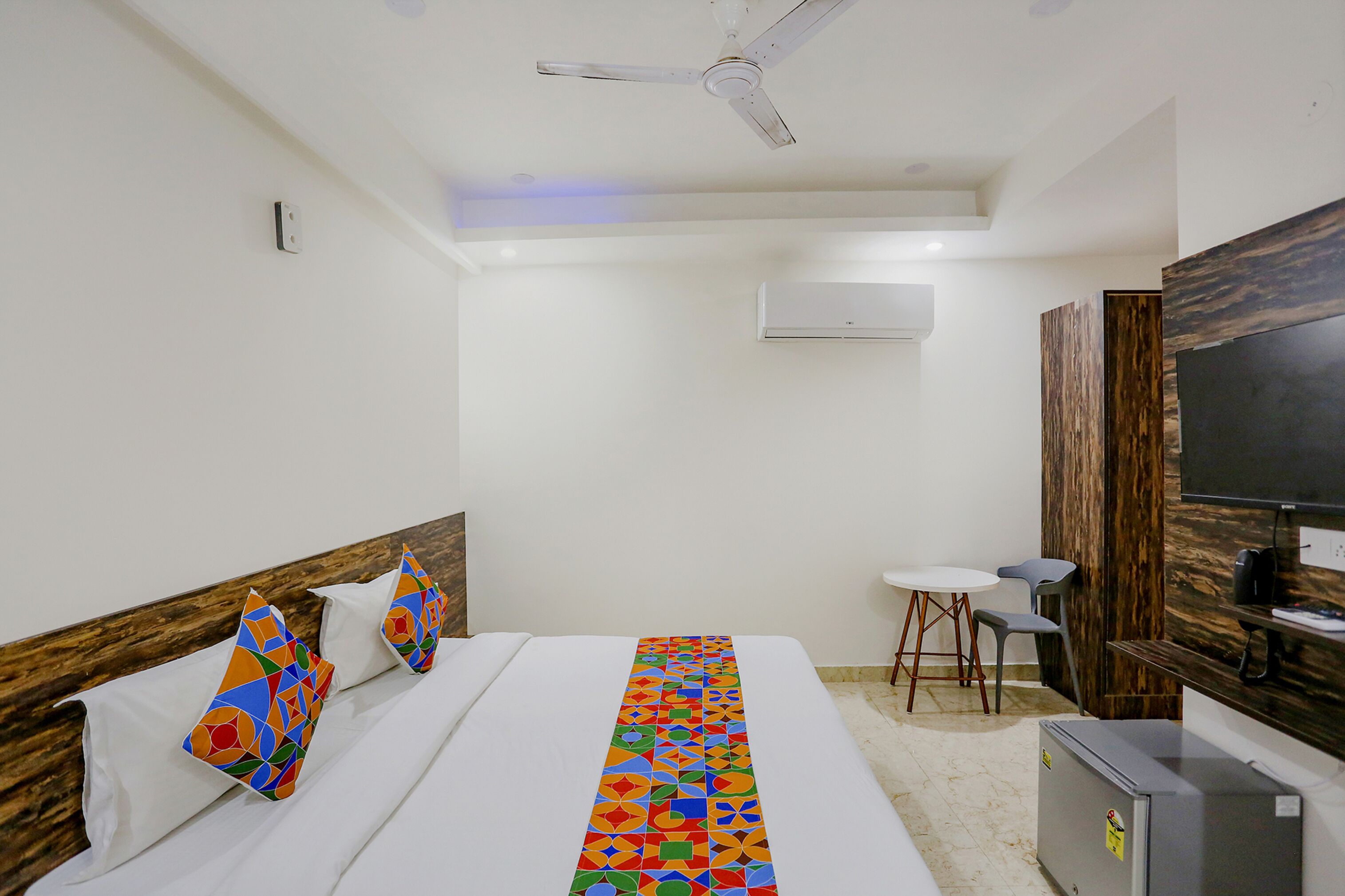 A hotel room with a bed, a desk, a chair, a television, and an air conditioning unit.