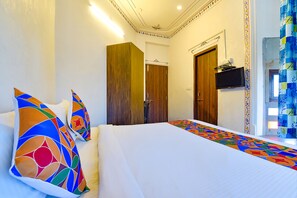 A hotel room with a large bed, colorful pillows, a TV mounted on the wall, and a door leading to another room.