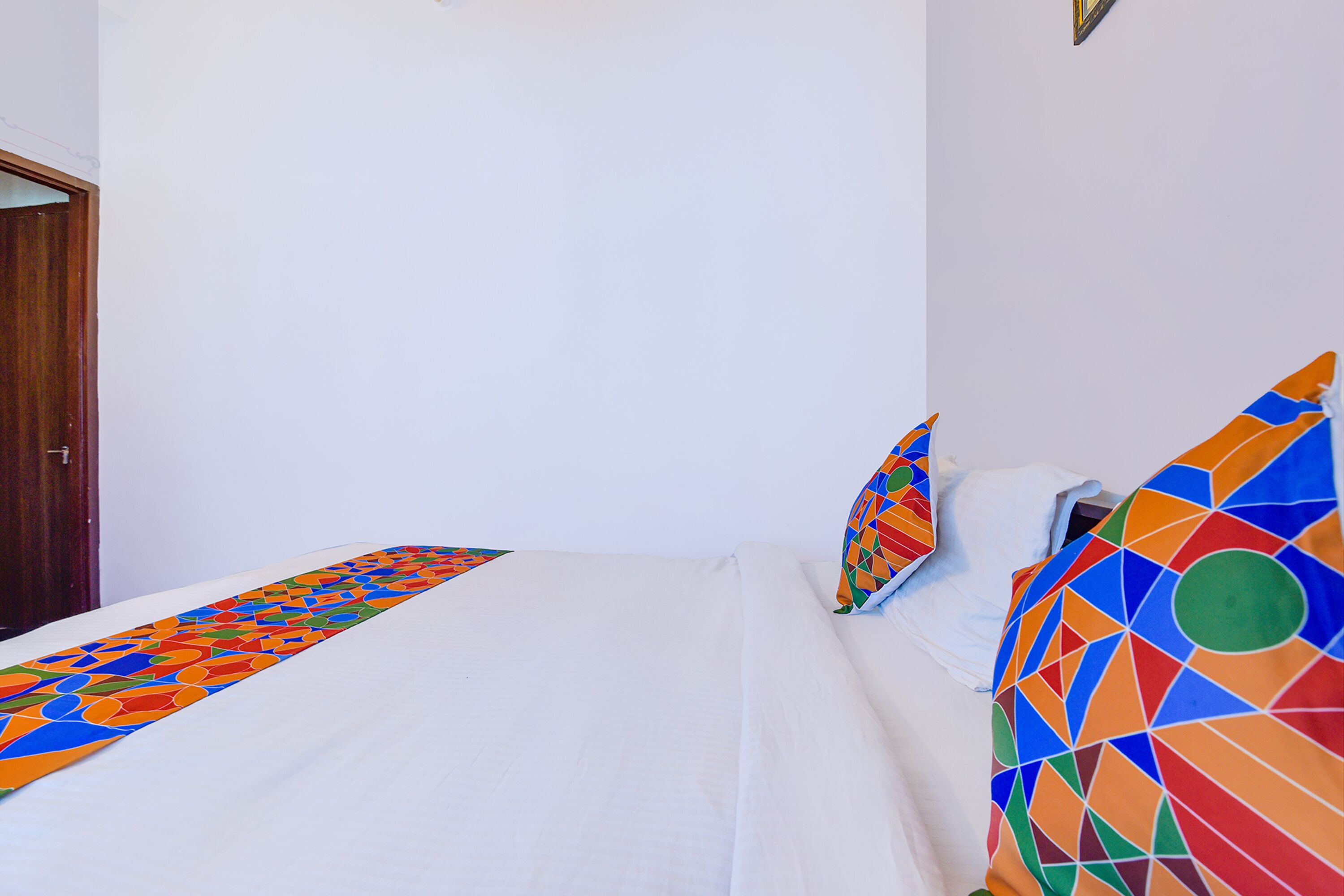 Una cama con sábana blanca y almohadas geométricas de colores.