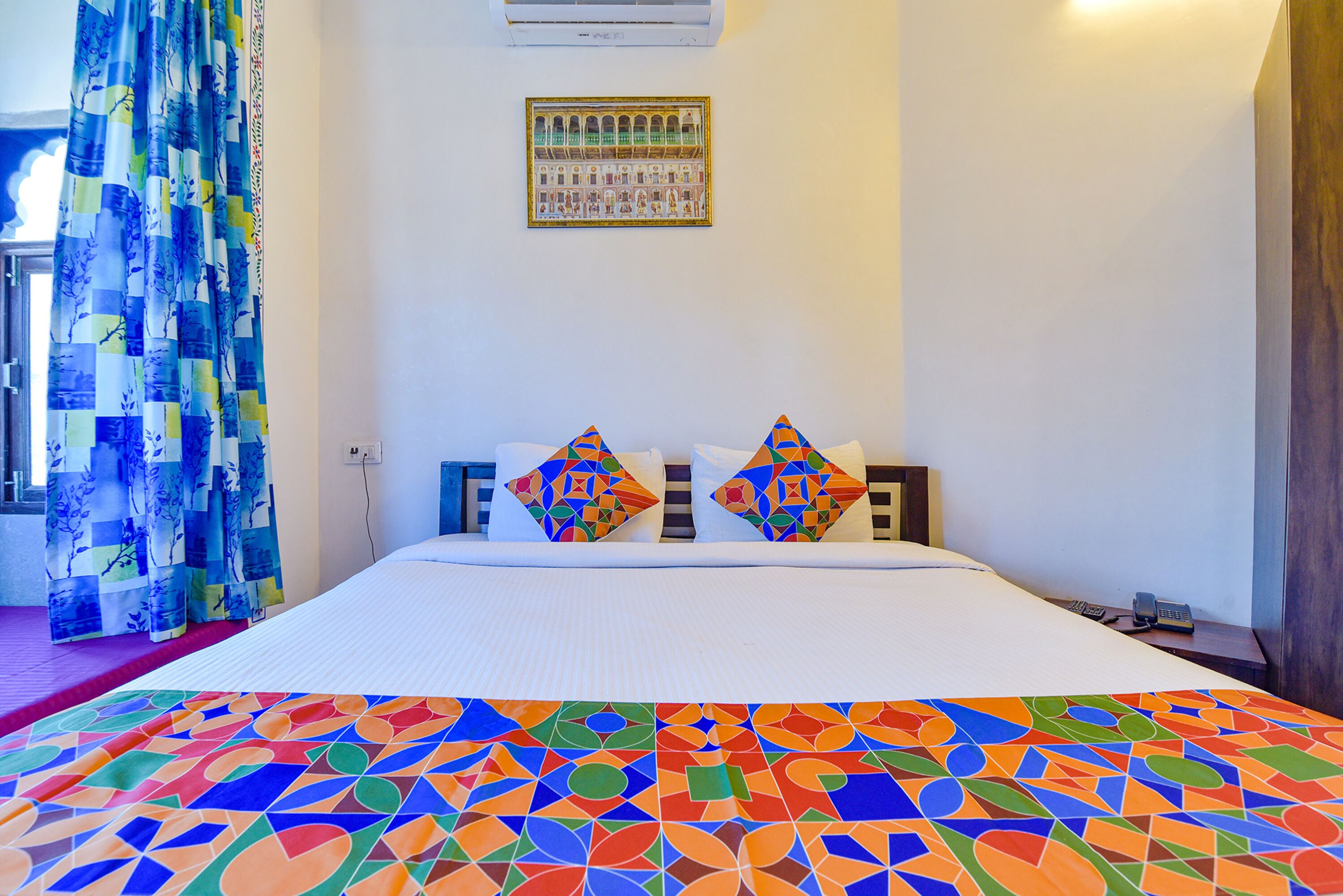 A hotel room with a bed, colorful curtains, a patterned bedspread, and a framed picture on the wall.