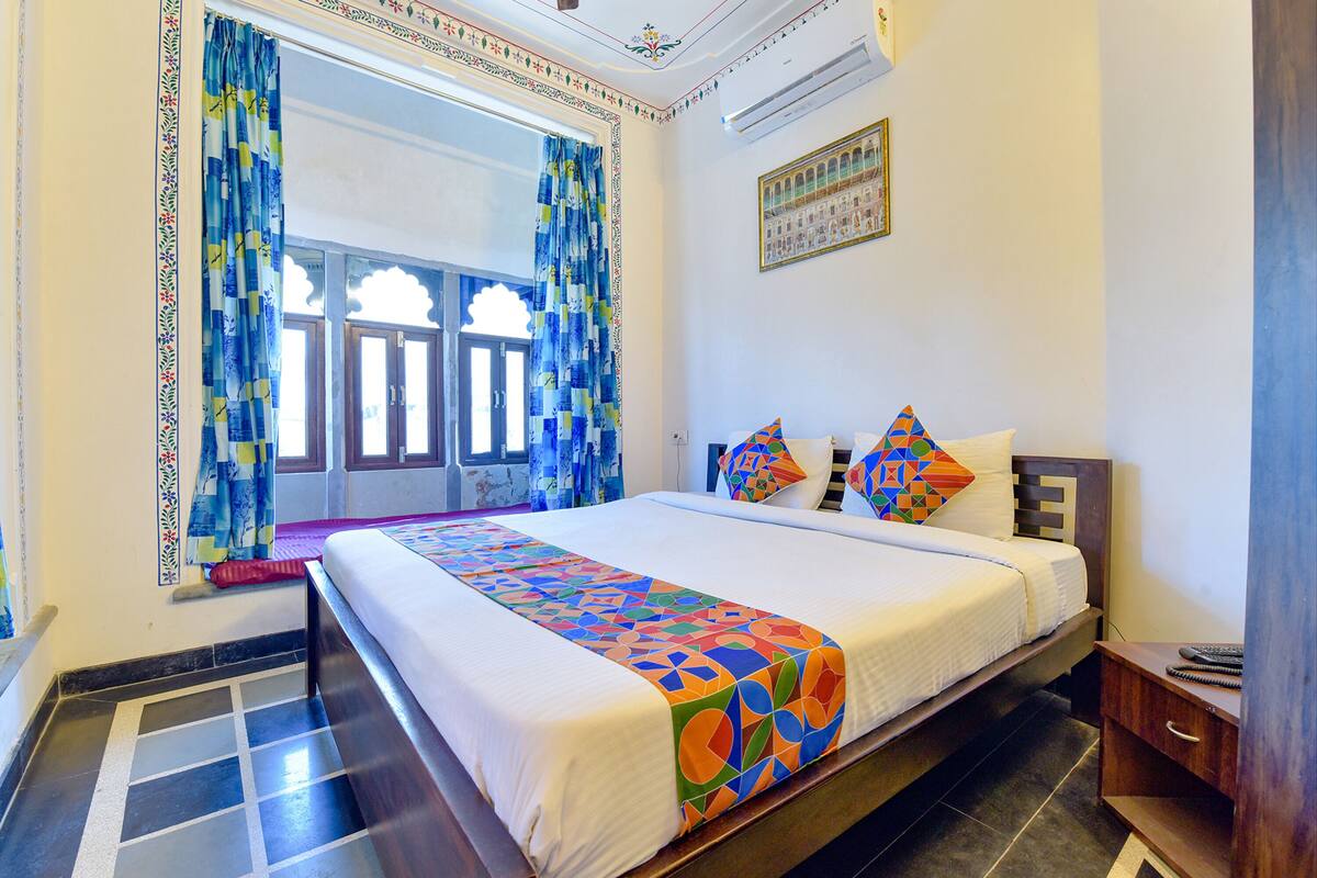 Una habitación de hotel con una cama grande, una mesita de noche de madera y una ventana con cortinas.