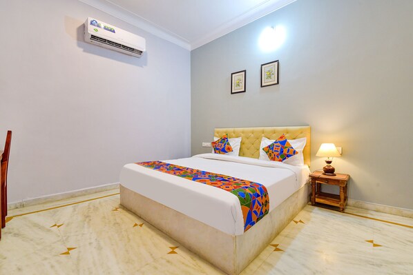 A hotel room with a bed, a bedside table with a lamp, an air conditioner, and a wall-mounted picture frame. - Fabhotel The Castle Homestay I (Udaipur)