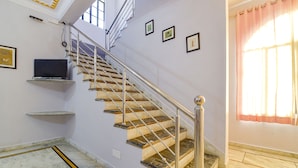 A staircase with marble steps and metal railings, a flat-screen TV mounted on a shelf, and framed pictures on the wall. - Fabhotel The Castle Homestay I (Udaipur)
