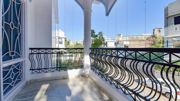 A balcony with a metal railing, white columns, and a view of buildings and trees. - Fabhotel The Castle Homestay I (Udaipur)