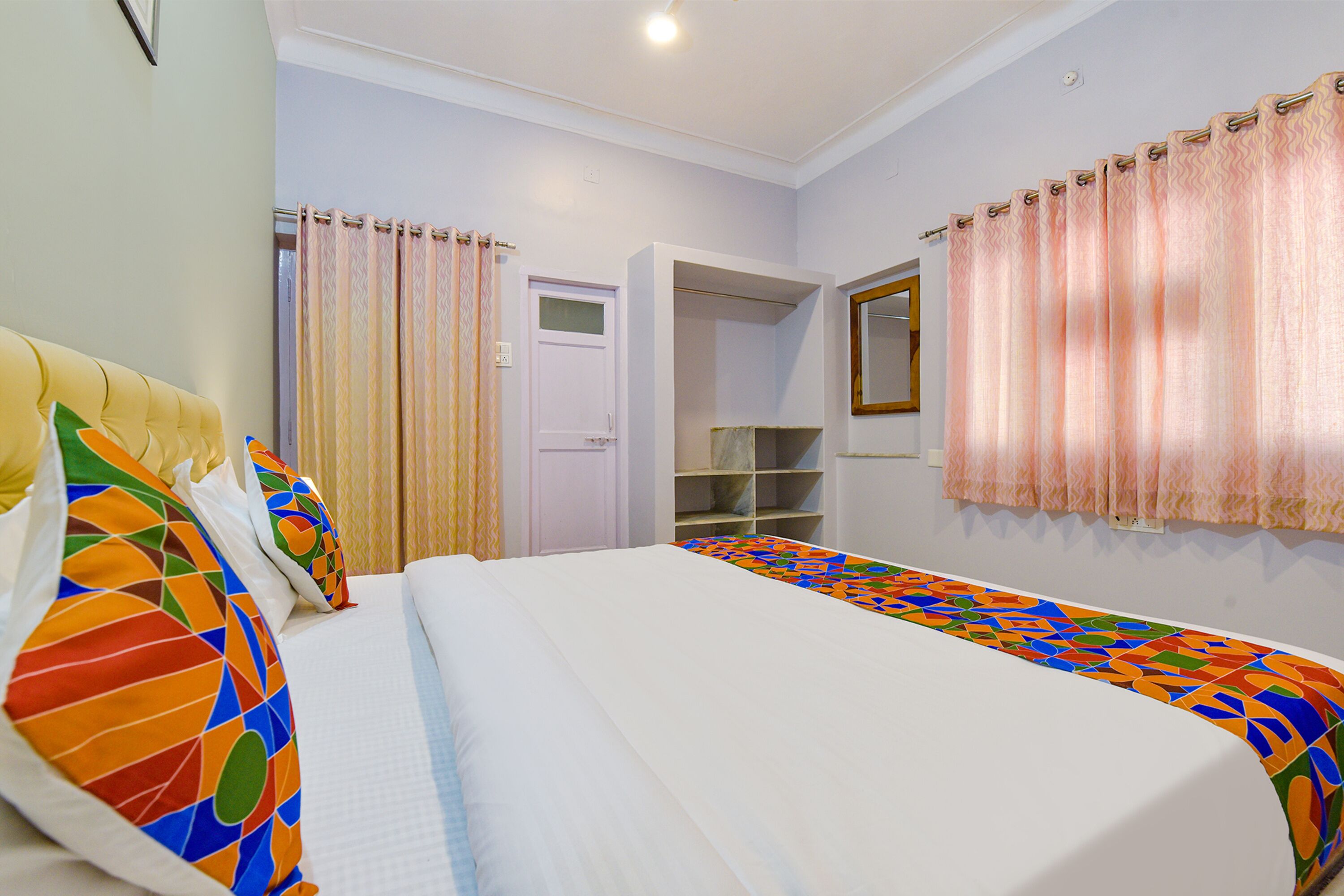A bedroom with a bed, colorful pillows, a wardrobe, and a mirror.