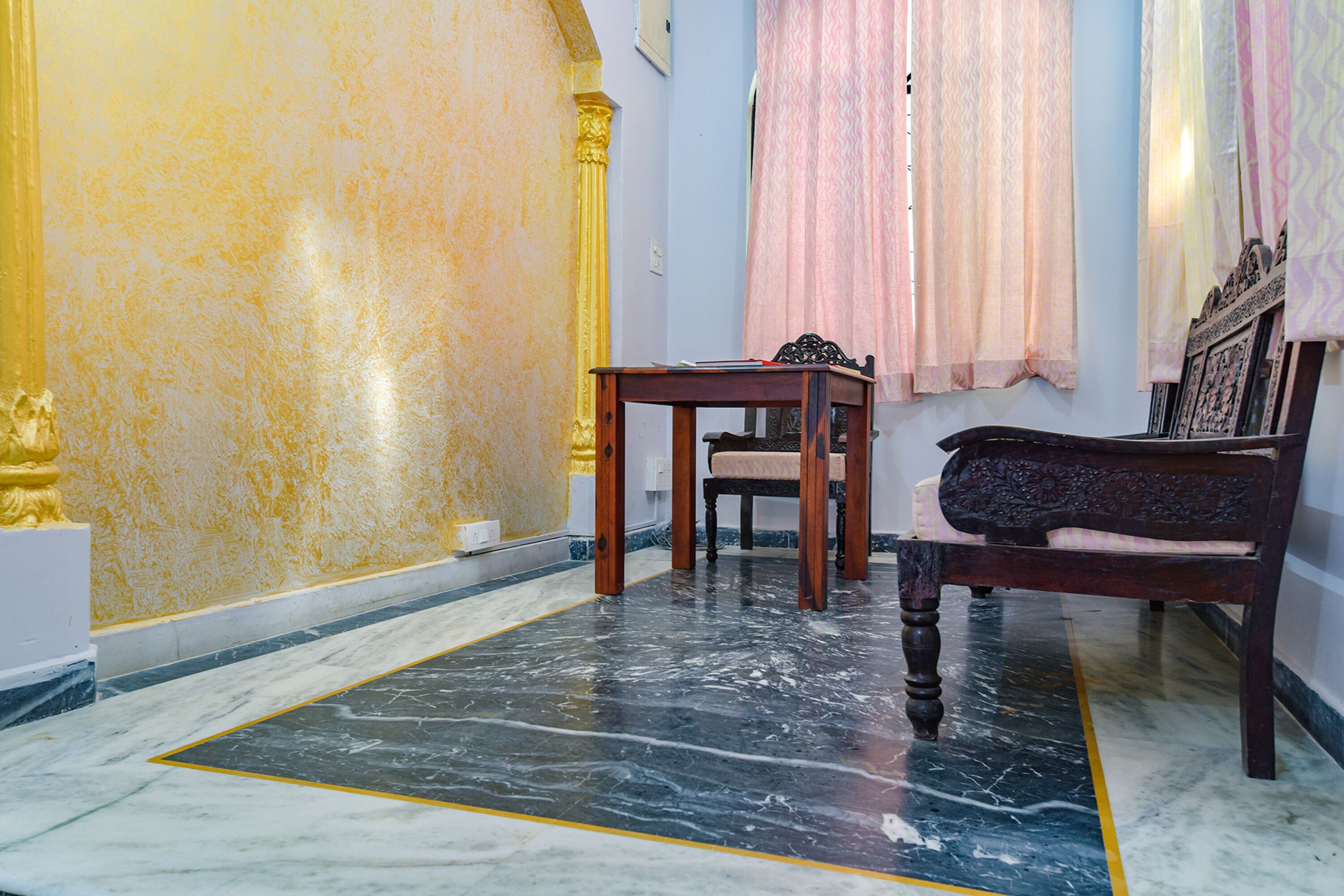 Una habitación con piso de mármol, una mesa de madera, un banco y una pared con molduras decorativas.