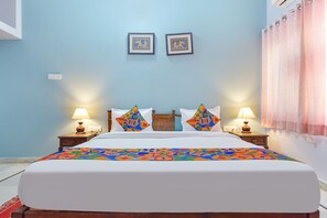 A neatly made bed with a colorful geometric-patterned bedspread, two bedside lamps, and two framed pictures on the wall.