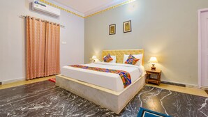 A hotel room with a bed, curtains, a nightstand, a lamp, and an air conditioning unit. - Fabhotel The Castle Homestay I (Udaipur)