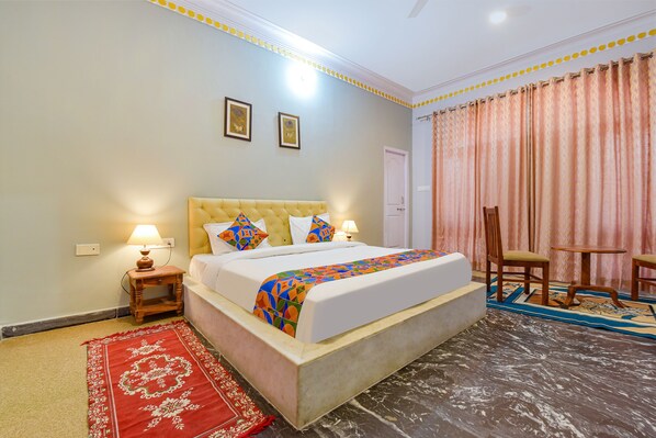 A hotel room with a bed, two bedside lamps, a red and white patterned rug, a wooden chair, and a small table.
