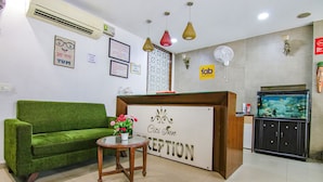 A reception area with a green sofa, a small table with a flower vase, and a reception desk with a sign that reads "Citi Sun Reception". - Fabhotel Citi Inn (Dera Bassi)