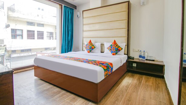 A hotel room with a large bed, a wooden floor, a view of buildings outside, and a small table with bottles. - Fabhotel Citi Inn (Dera Bassi)