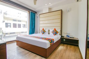 A hotel room with a large bed, a wooden floor, a view of buildings outside, and a small table with bottles. - Fabhotel Citi Inn (Dera Bassi)