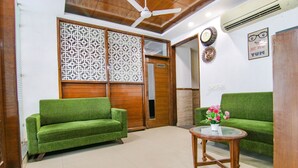 A room with two green sofas, a wooden coffee table with a vase of flowers, a ceiling fan, and a wall-mounted air conditioner. - Fabhotel Citi Inn (Dera Bassi)