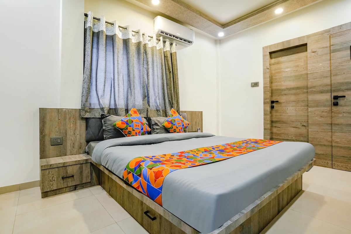 Un dormitorio con cabecera de madera, una cama con colcha de diseño geométrico y colores vivos, una mesita de noche y un armario de madera.