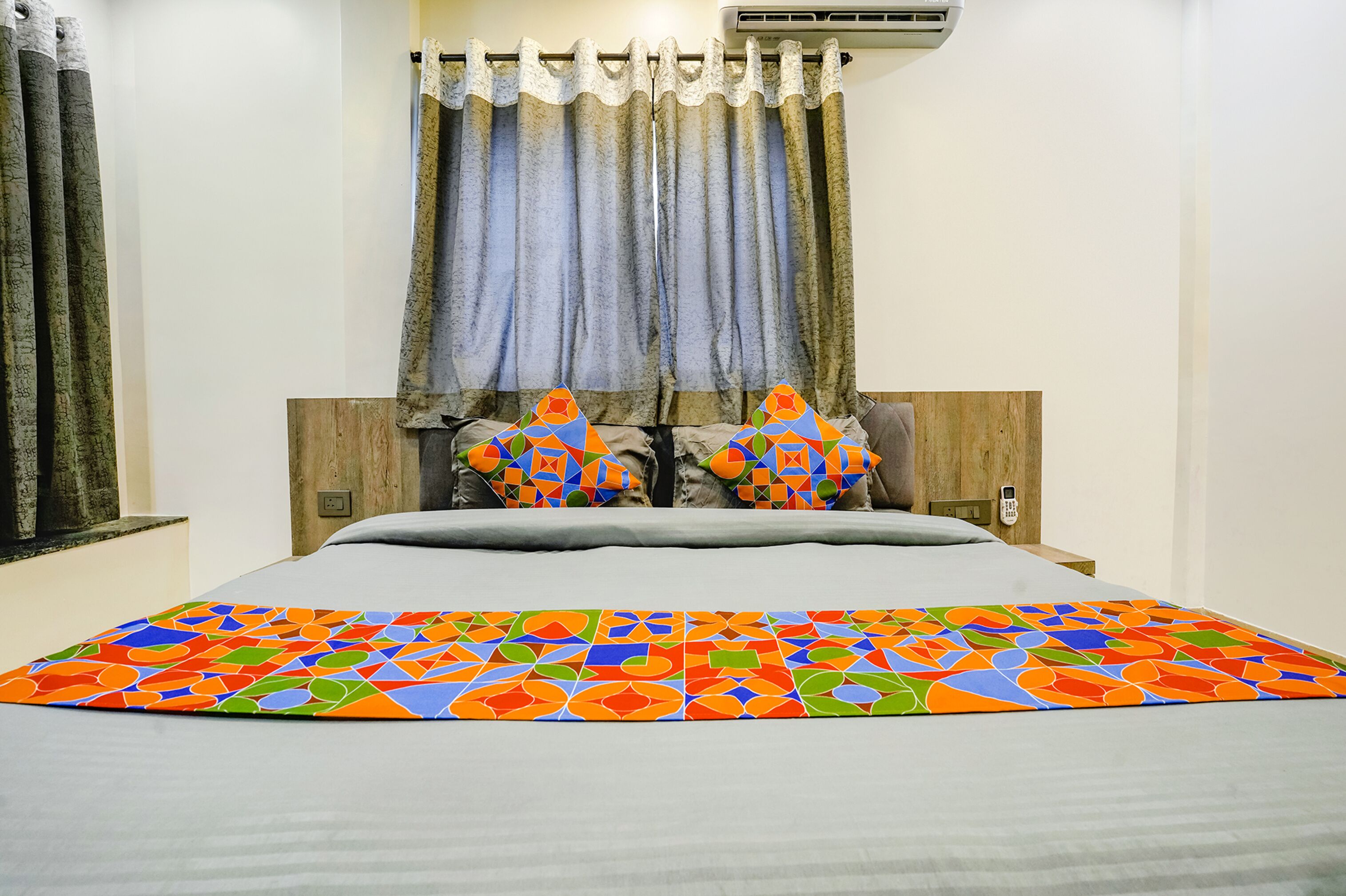 A neatly made bed with a colorful geometric-patterned bedspread, a wooden headboard, and two decorative pillows.