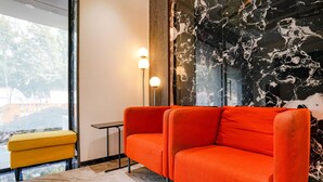A modern living room with a red sofa, a yellow ottoman, and a marble wall. - Fabexpress The Dream Residency (Mumbai)
