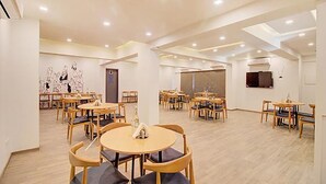 A spacious dining area with round tables and chairs, a large window, and a wall with abstract art. - Fabhotel Ashray Residency (Navi Mumbai)